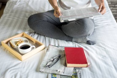 Kitap ya da gazete okuyan ve sabahları yatakta kahve içen bir kadın.