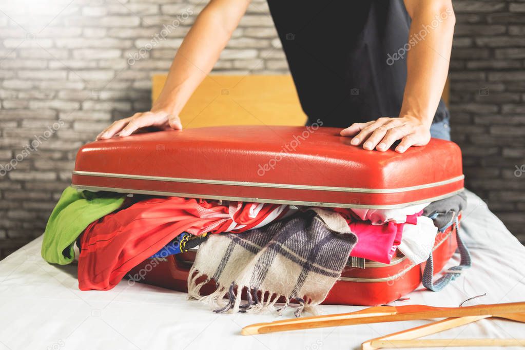 man trying to fit all clothing to packing his red suitcase before vacation