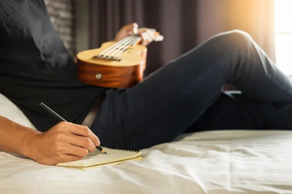 幸せな若いアジア男の寝室のベッドの上に座ってウクレレを演奏 — ストック写真