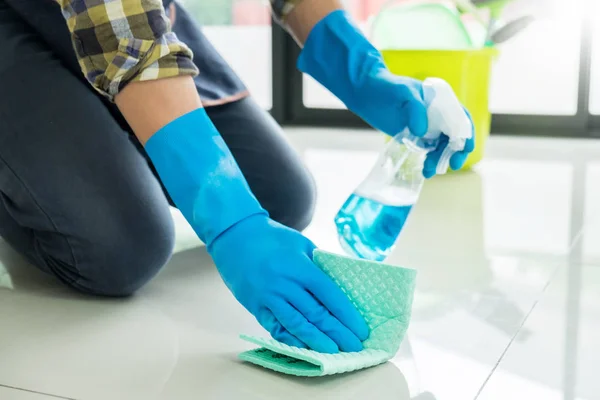 man with cloth cleaning floor in home uses rag and fluid in a spray.
