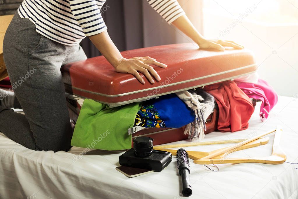 Woman trying to fit all clothing to packing her red suitcase before vacation