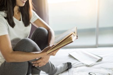 Kitap ya da gazete okuyan ve sabahları yatakta kahve içen bir kadın.
