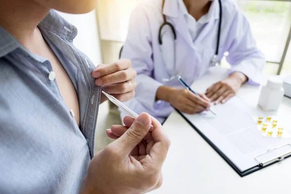 Doctor with a thermometer in his hand taking patient\'s in hospital, medical concept.