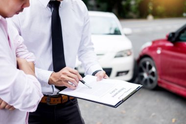 Insurance agent writing on clipboard while examining car after accident claim being assessed and processed clipart