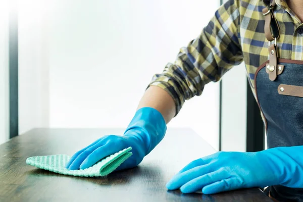 man with cloth cleaning wooden table in home uses rag and fluid in a spray