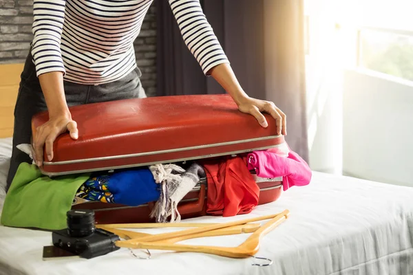 Woman trying to fit all clothing to packing her red suitcase before vacation