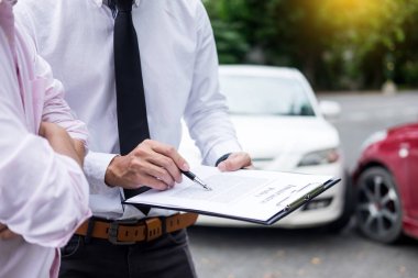 Insurance agent writing on clipboard while examining car after accident claim being assessed and processed clipart