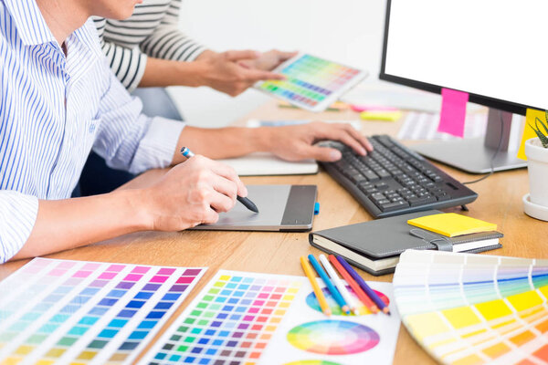 дизайнер графического творчества, работающий вместе с раскраской с помощью графического планшета и стилуса за столом с коллегой
 