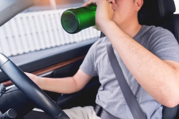 ドライブの概念のために飲んではいけない、若い酔った男は、危険な車を運転中にビールやアルコールのボトルを飲みます. — ストック写真