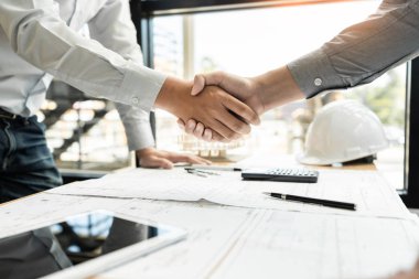 Mimar ve mühendis inşaat işçileri ofis inşaatındaki bir anlaşmayı bitirdikten sonra takım çalışması ve işbirliği konsepti için çalışırken el sıkışıyorlar, başarı işbirliği konsepti 