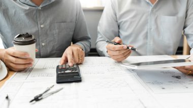 Mimari ekipmanlarla çalışan kendine güvenen mühendis ekibi iş akışı inşaatı projesini tartışıyor ve planlıyor. Ofis şantiyesindeki masada ortağıyla..