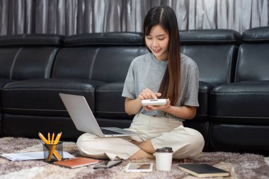 Çekici genç Asyalı kadın girişimci ya da evde dizüstü bilgisayarla çalışan serbest çalışan iş raporları ve oturma odasındaki kanepede internetten iletişim kuran, uzaktan erişim kavramına uzaktan erişen 