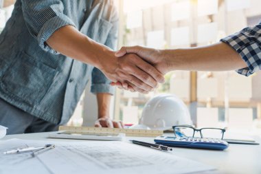 Mimar ve mühendis inşaat işçileri ofis inşaatındaki bir anlaşmayı bitirdikten sonra takım çalışması ve işbirliği konsepti için çalışırken el sıkışıyorlar, başarı işbirliği konsepti