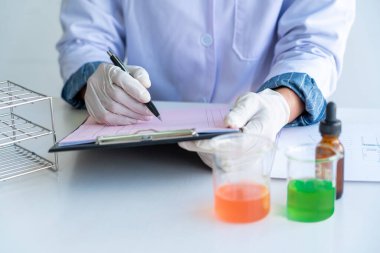 Laboratuvarda beyaz önlükle araştırma yapan bilim adamları eldivenleri analiz ediyor, test tüpleri örneklerine bakıyor, biyoteknoloji kavramına bakıyor..