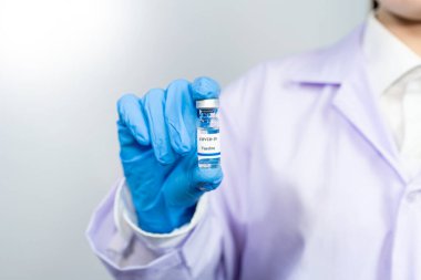Coronavirus aşısı COVID-19 şişesi koruyucu giysi içinde doktor veya teknisyen bilim adamı, antiviral sağlık ve tıbbi biyolojik tehlike konsepti.