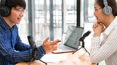 Asyalı kadın radyo sunucuları stüdyoda bir erkekle röportaj yaparken stüdyoda canlı yayın için podcast yaparken mikrofona el kol hareketi yapıyorlar..