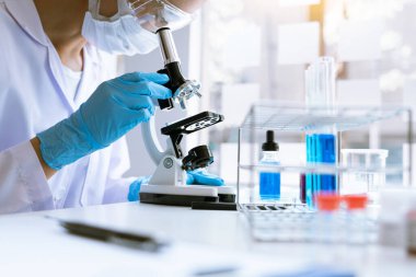 Genç Asyalı bilim adamı mikroskopla inceleyerek adli tıp laboratuarındaki bir deney örneğini analiz ediyor.