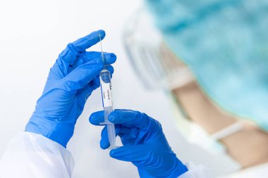 Doktor, bilim adamı, mavi eldivenli bir araştırmacı ya da koruyucu giysi giymiş. İnsan klinik enjeksiyon deneylerine hazırlanıyor. Cvid-19 Coronavirus aşısı biyolojik tehlike kavramı.
