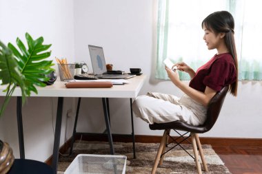 Çekici genç Asyalı kadın girişimci ya da evde dizüstü bilgisayarla çalışan serbest çalışan iş raporları ve oturma odasındaki kanepede internetten iletişim kuran, uzaktan erişim kavramına uzaktan erişen