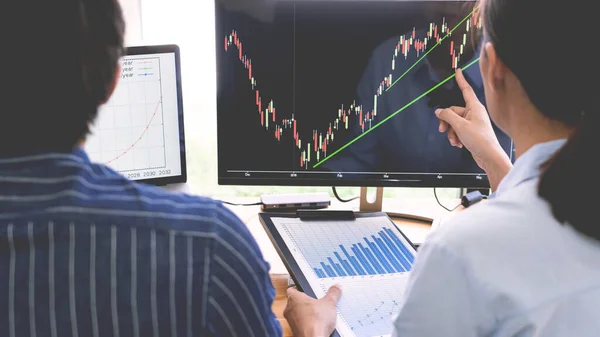broker showing some ascending to his colleague planning and analyzing graph stock market trading with stock chart data on multiple computer screens