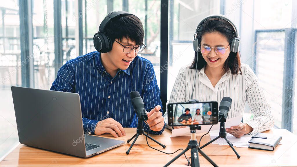 Asian Man and woman podcasters in headphones recording content with colleague talking to microphone and camera in broadcast studio together, communication technology and entertainment concept