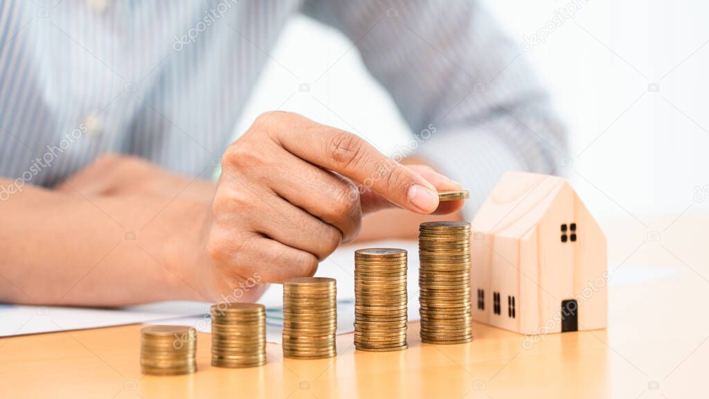 Property investment and house mortgage financial concept, hand of a businessman who is stacking coins for Real estate investment, saving for buying for housing or speculation