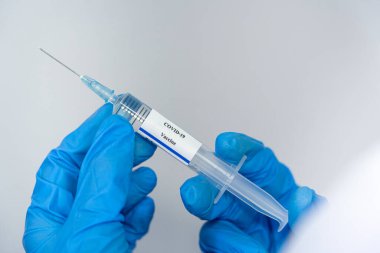 Doktor, bilim adamı, mavi eldivenli bir araştırmacı ya da koruyucu giysi giymiş. İnsan klinik enjeksiyon deneylerine hazırlanıyor. Cvid-19 Coronavirus aşısı biyolojik tehlike kavramı.