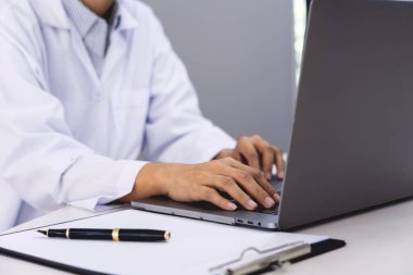 Laptop bilgisayarla çalışan doktor hastane ofisinde ya da klinikte oturuyor, sağlık hizmetleri ve tıbbi teknoloji konsepti
