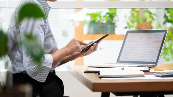 women holding smartphone getting message making transaction on laptop computer at modern loft wooden desk in office