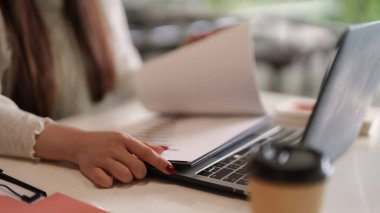 Yetişkin el önemli iş belgelerini bir dizüstü bilgisayarın yanında inceler. Çağdaş ofis ortamında görevleri etkili bir profesyonel yönetir.