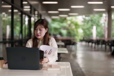 Odaklanmış Asyalı kadın laptopta çalışıyor ve dışarıda veri analizi yapıyor. İş stratejileri planlar, hedeflerine ulaşır ve uzaktan başarılı olur..