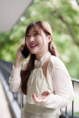 Genç Asyalı serbest çalışan kadın dışarıda akıllı telefondan konuşuyor. Neşeli ifade, profesyonel uzaktan kumandalı mobil teknoloji bağlantısı.