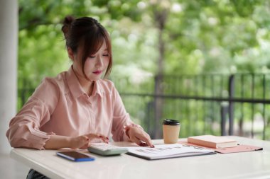 Yetişkin Asyalı kadın finansal hesaplamalar yapıyor iş raporlarını analiz ediyor sakin doğa görüşlerinin keyfini çıkarıyor üretkenlik iş dengesini artırıyor