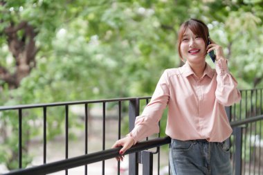 Genç Asyalı kadın cep telefonuyla iletişim kuruyor. Temiz havanın tadını çıkarıyor. Uzaktan kumandalı iş. Modern yaşam tarzı.