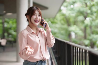 Neşeli Asyalı kadın açık havada uzaktan çalışmayı konuşuyor. Profesyonel bağlantıyı, hayat dolu bir yaşam tarzını ve geleneksel bir ofisten kurtulmayı seviyor..