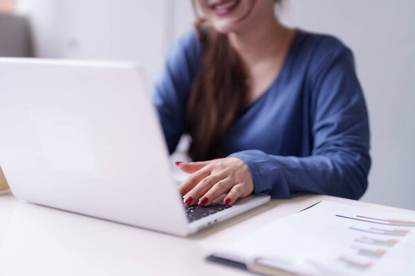 Улыбающаяся взрослая азиатка работает с ноутбуками и деловыми документами. Профессиональный фрилансер наслаждается удаленной онлайн-карьерой из современного офиса.