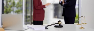 Law experts convene discussing important legal paperwork. Symbols of justice gavel scales adorn desk. Professional office environment.
