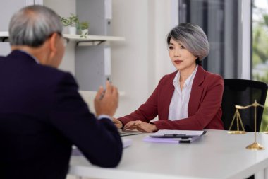 Adult Asian female attorney offers legal counsel to client at desk in contemporary office. Professional discussion and strategic advice.