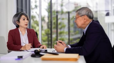 Asian adult legal professionals discuss important matters in a modern office. They review paperwork providing expert advice and strategic solutions. Focused meeting.