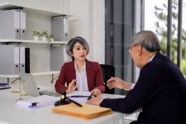 Asian adult legal professionals engaging in serious discussion. They review documents seeking expert advice. This professional office meeting embodies justice principles. One participant is partially blurred.