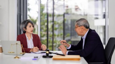 Two Asian legal professionals discuss serious matters in a modern office. They offer expert advice with justice symbols present