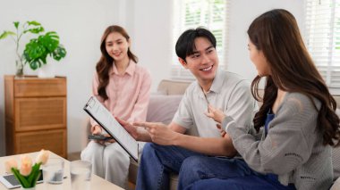 Expert Asian insurance agent provides personalized health coverage consultation to a couple within their living room explaining policy details
