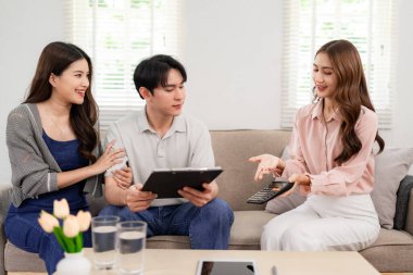 Professional Asian woman offers health policy advice to young adult couple comfort living room setting expert consultation financial security guidance