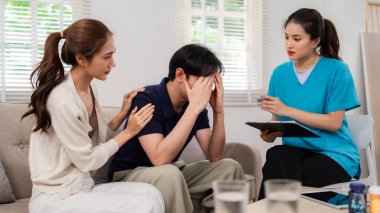 Asian man deeply distressed seeking professional mental health guidance with wife support during home therapy session for improved well-being