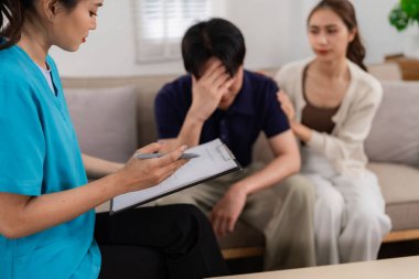 Healthcare professional offers mental wellness advice to couple. Man experiencing emotional distress finds comfort from partner during home consultation.