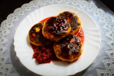 Koyu kahverengi bir masada tatlı lezzetli Kahvaltı, beyaz desenli masa örtüsü, beyaz yuvarlak tabakta. Ahududu reçeli ile taze lor peynirli kek. Tatlı, fırında pişmiş