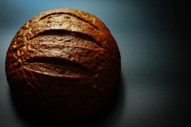 Ekmek siyah bir arka plan üzerinde yatıyor, üst görünümü. Ekmek taze ve yuvarlak bir şekli vardır. Ekmek buğday unundan yapılır