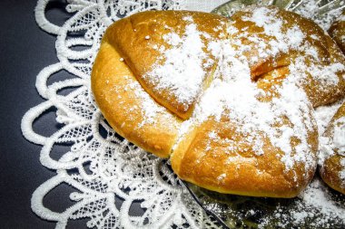 Kahverengi bir masada beyaz bir masa örtüsünün üzerinde cam bir tabakta çay için tatlı bir çörek var.