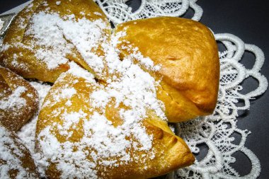 Masa örtüsünün üzerindeki siyah arka planda elma ve pudra şekeriyle doldurulmuş beyaz bir çörek var.