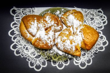 Siyah bir arka planda, cam bir tabakta, elma reçelli iki taze çörek, pudra şekerinin üstünde.